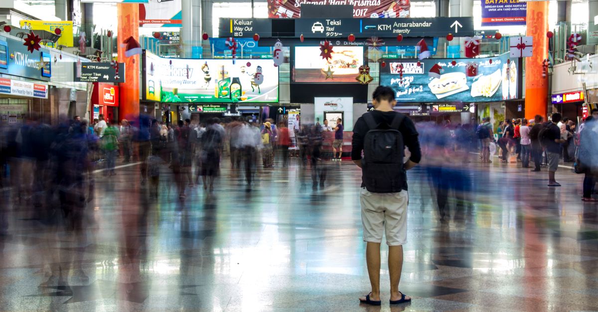 Voyageur avec un sac à dos dans le hall de la gare KL Sentral, sous les panneaux KTM et KLIA Ekspres