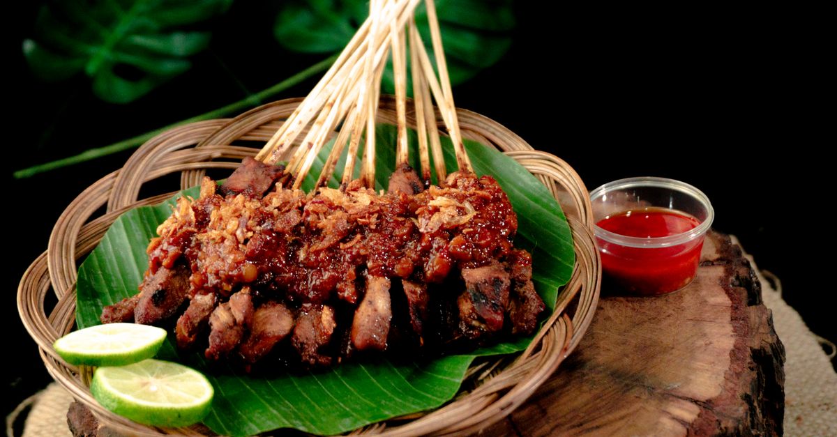 Brochettes de viande grillée nappées de sauce, servies sur une feuille de bananier avec du citron vert