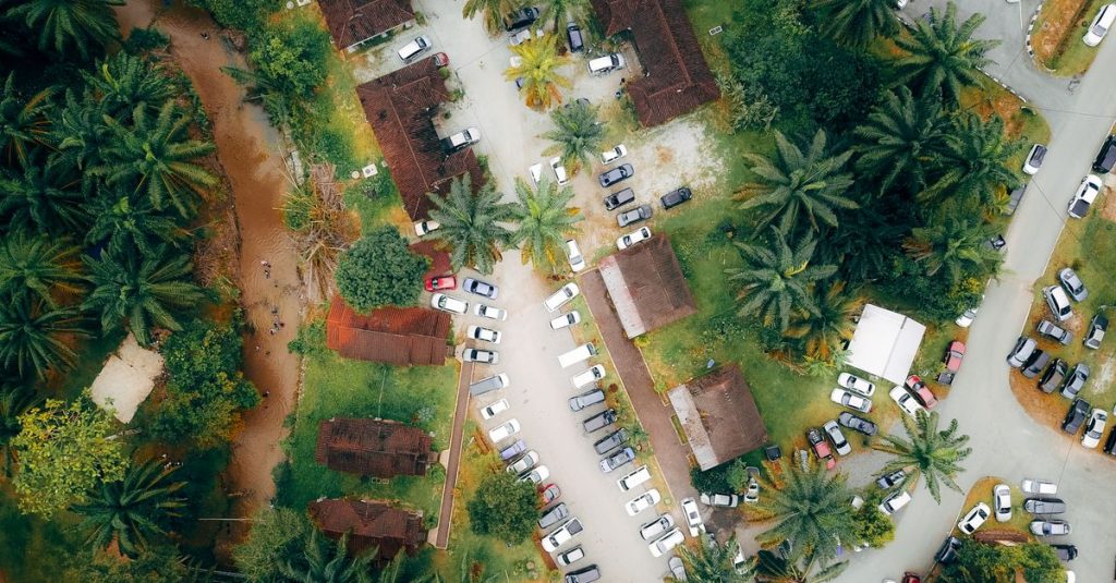 Vue aérienne d’un village entouré de palmiers, avec des toits de tuiles et un parking