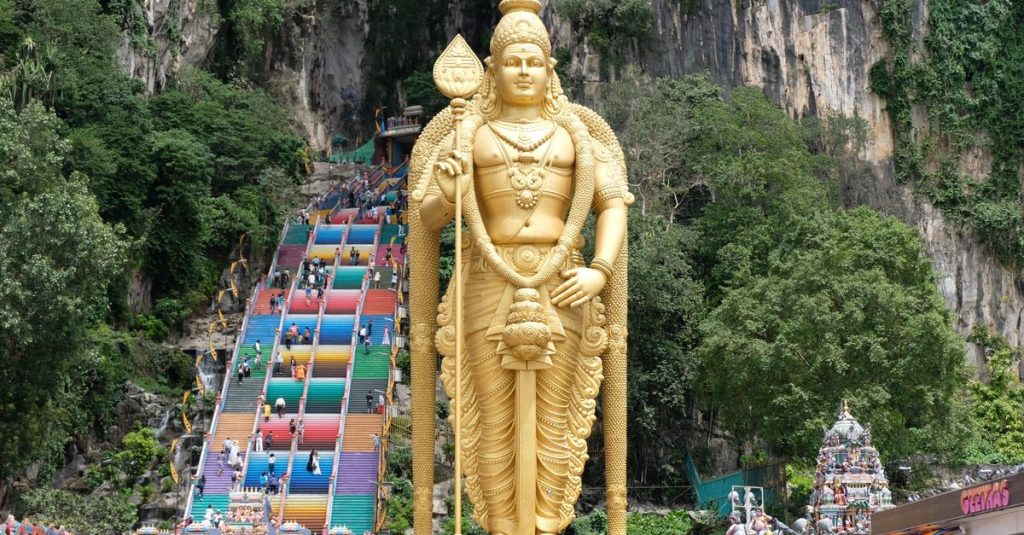 Statue dorée de Murugan devant l’escalier coloré des grottes de Batu Caves, près de Kuala Lumpur, avec des visiteurs sur les marches